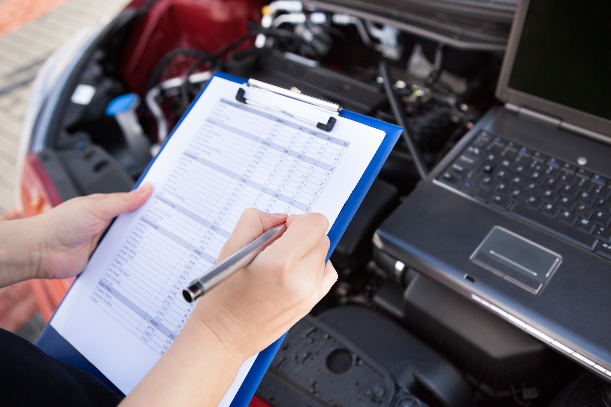 Vehicle technician using clipboard to take notes on vehicle